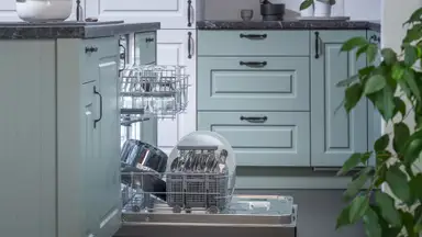 Hisense HUI6220XCUS dishwasher review—Pictured is a shot of the Hisense HUI6220XCUS dishwasher installed into a typical kitchen, from a side angle. Its door is open and its racks have been pulled out slightly. Both racks are stocked with dishes.