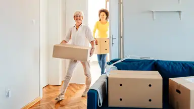 Two people holding boxes move into a new apartment.