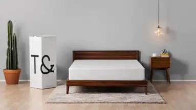 A bare Tuft and Needle mattress, sitting on a wooden bed frame in a master bedroom.