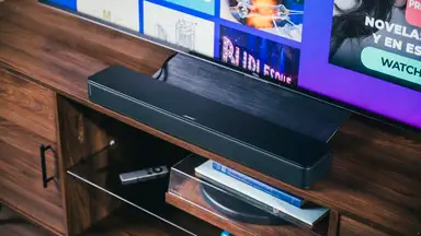 The Bose TV Speaker sits perfectly under a TV, set in all black on a rich wooden cabinet above a record player and other accessories.