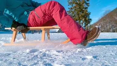 A model wearing snow pants glides across a frozen lake on a sled.