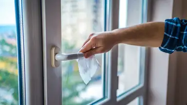 A man cleans a door handle with a disinfecting wipe