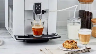 Close-up photo of a Jura high-end coffee maker in action. A scone sits on a small plate beside it.