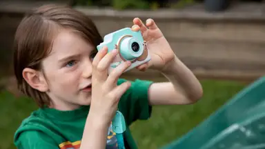 A young child happily takes a photo with their Kidamento kids digital camera