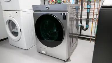 Product shot of the stainless steel Samsung Bespoke WF53BB8700AT front-load washer machine inside inside of testing lab.