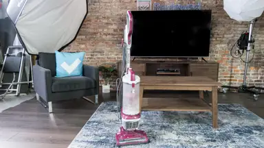 A red upright vacuum stands on a blue carpet