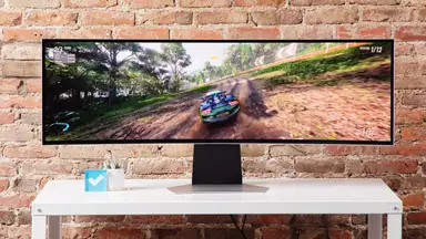 The Samsung’s Odyssey OLED G9 on a white table with a brick background.