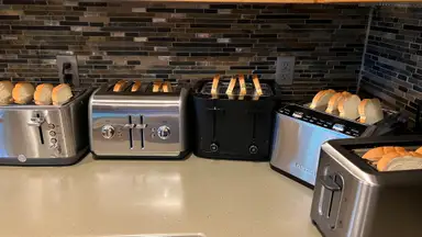 Five 4-slice toasters filled with bread slices on a countertop
