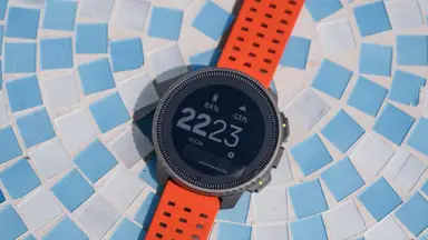 The Suunto Vertical Titanium Solar outdoor watch sits on a blue mosaic tabletop