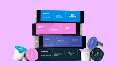 An image of a stack of Cometeer coffee boxes in shades of blue, pink, and purple, surrounded by Cometeer coffee pods in the same colors.