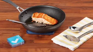 Seared salmon in Circulon ScratchDefense skillet, surrounded by metal utensils and a Reviewed checkmark.
