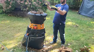 A person outdoors putting leaves into the top of the Worx Electric Leaf Mulcher with a large contractor garbage bag attached to the stand below it.