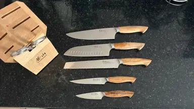 Five Cangshan knives laid out on black countertop beside the wooden knife block.