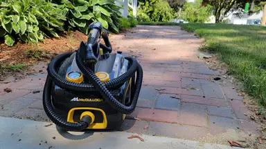 A black and yellow steam cleaner sits on a brick walkway out of doors and next to a green lawn