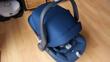 The Uppababy Mesa Max car seat in navy blue with hooded shade pulled all the way down on top of hardwood floor.