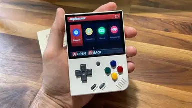 A hand holds the Miyoo Mini Plus with the home screen showing.