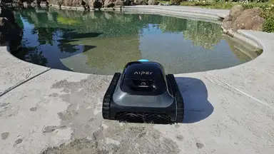The Aiper Scuba S1 pool cleaner on a concrete pool deck outdoors.