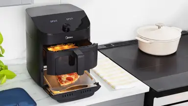 Midea air fryer on a kitchen counter with pizza cooking in bottom section and fries cooking in top basket