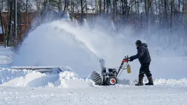 A person in winter wear puts their snow blower to good use following a heavy snowfall.
