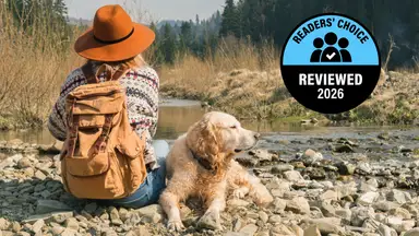 Person sitting beside a dog by a rocky stream with a Reviewed Readers' Choice 2026 badge displayed.