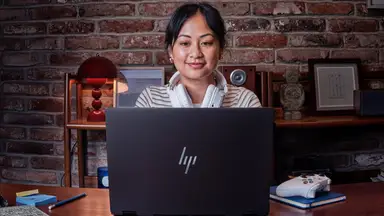 Person wearing headphones and using an HP laptop at a desk with a game controller nearby.