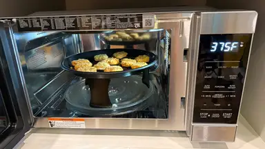 Stainless steel Sharp 900W Countertop Convection Microwave open and showing chicken nuggets inside.