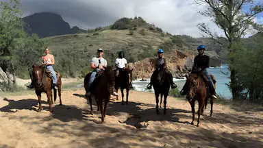 Group of people riding horses along a scenic beach trail with ocean cliffs in the background.