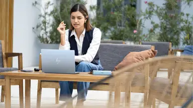 Woman sitting in front of silver HP laptop on a wooden table.