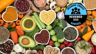 An overhead view of fresh vegetables, legumes, and spices arranged on a dark surface, with a "Readers' Choice Reviewed 2026 Nominee" badge.