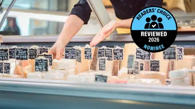A deli case with an assortment of labeled cheeses, with a "Readers' Choice Reviewed 2026 Nominee" badge.