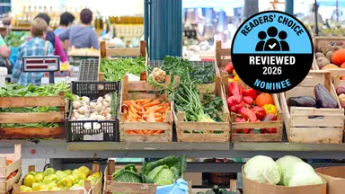A market stall displaying berries, pineapples, and other fresh produce in baskets, with a "Readers' Choice Reviewed 2026 Nominee" badge.