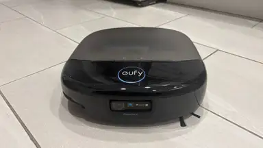 A black robot vacuum on a beige tile floor