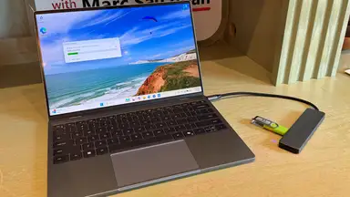Dell XPS 13 sitting on a wooden surface with a USB adapter and flash drive plugged into the right side.