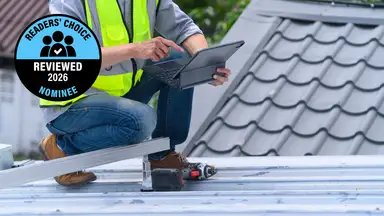 A person in a safety vest stands on a roof with a laptop