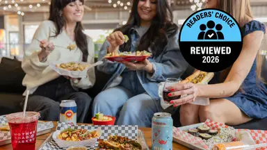Three woman sit on a couch eating food in a food hall environment