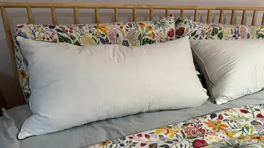 Two white Pacific Coast Feather & Down Pillows on a bed with floral sheets and a wooden barred headboard.