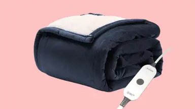 A folded blue electric blanket with a white sherpa lining is shown against a pink background.