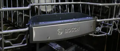 A close-up of the front of a Bosch dishwasher's top rack, which has the Bosch logo on it.