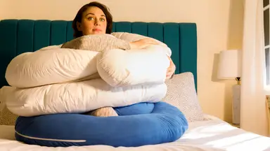 Writer Steph Garcia sits on a bed surrounding by pregnancy pillows.