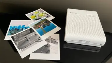 The Canon Selphy portable photo printer on a table next to some photographs.