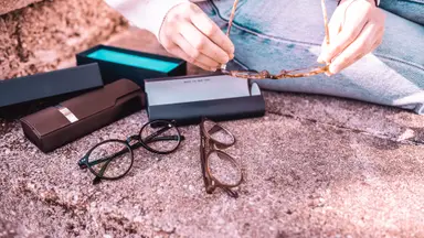 Two pairs of glasses and their boxes are spread out on a sidewalk while a woman holds a third pair.