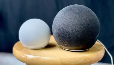 Two Echo Dot speakers, one white and one black, sitting atop a stool alongside each other.
