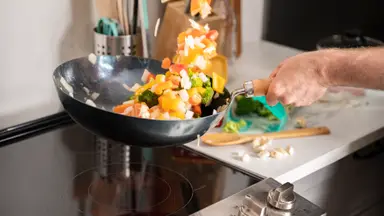 A person is stir frying a medley of vegetables in a carbon steel wok over an electric cooktop.