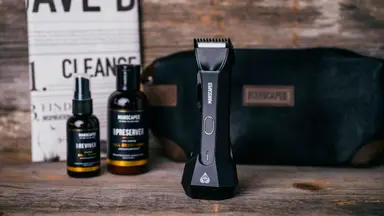 The contents of the Manscaped Perfect Package, which includes the trimmer, two bottles of product, a fake newspaper, and a toiletry bag.