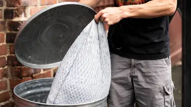 A person putting a trash bag inside of a garbage can.