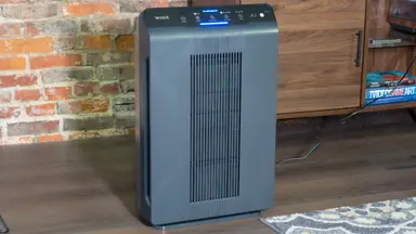 A black air purifier stands against a brick wall