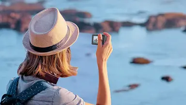 A woman using her waterproof camera at the beach on her family vacation.