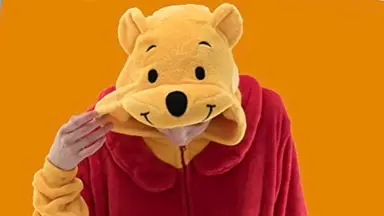 A person modeling their Winnie the Pooh costume onesie against a Halloween-orange backdrop.
