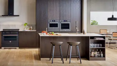 A lovely earthtone-themed kitchen with hardwood floors. There is a kitchen island, a hanging lamp, and a Bosch wall oven along the far wall.