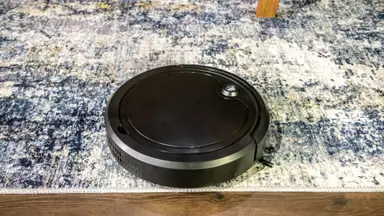 The Digital Essentials Robotic Vacuum Cleaner on a blue and white carpet.